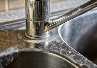 Close-up of a kitchen tap and sink with hard water calcification.